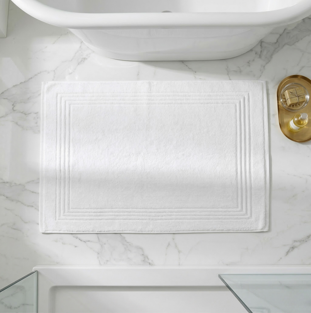 Alfombrilla de baño Blanc blanca de Morfeo con cenefa en relieve, sobre suelo de mármol junto a la bañera.