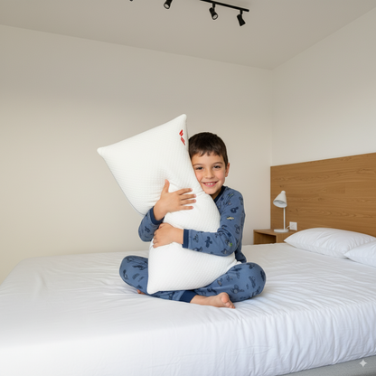Niño en pijama abrazando la almohada suave Calma de Morfeo sentado sobre la cama de un dormitorio.