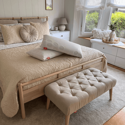 Banqueta Milos color beige de Morfeo con tapizado capitoné en ambiente de dormitorio colocada a los pies de la cama.
