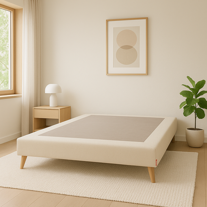Base tapizada Silos color beige de Morfeo en habitación luminosa con patas de madera, mesita, lámpara y planta.