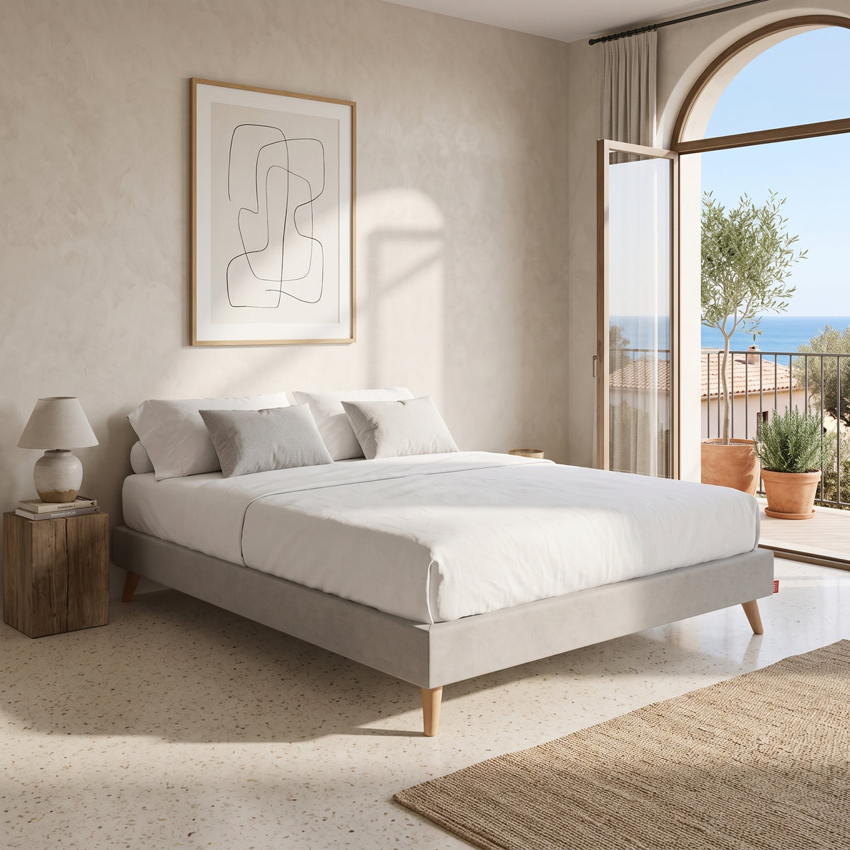 Base tapizada Silos color gris de Morfeo con patas de madera en dormitorio mediterráneo con vistas al mar.