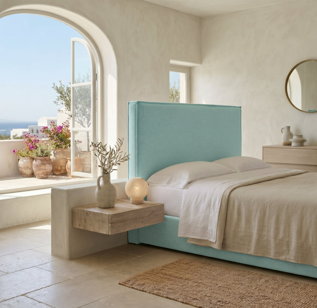 Cabecero tapizado Mox aguamarina de Morfeo, liso con vivo, en un dormitorio mediterráneo con arco y vistas al mar.