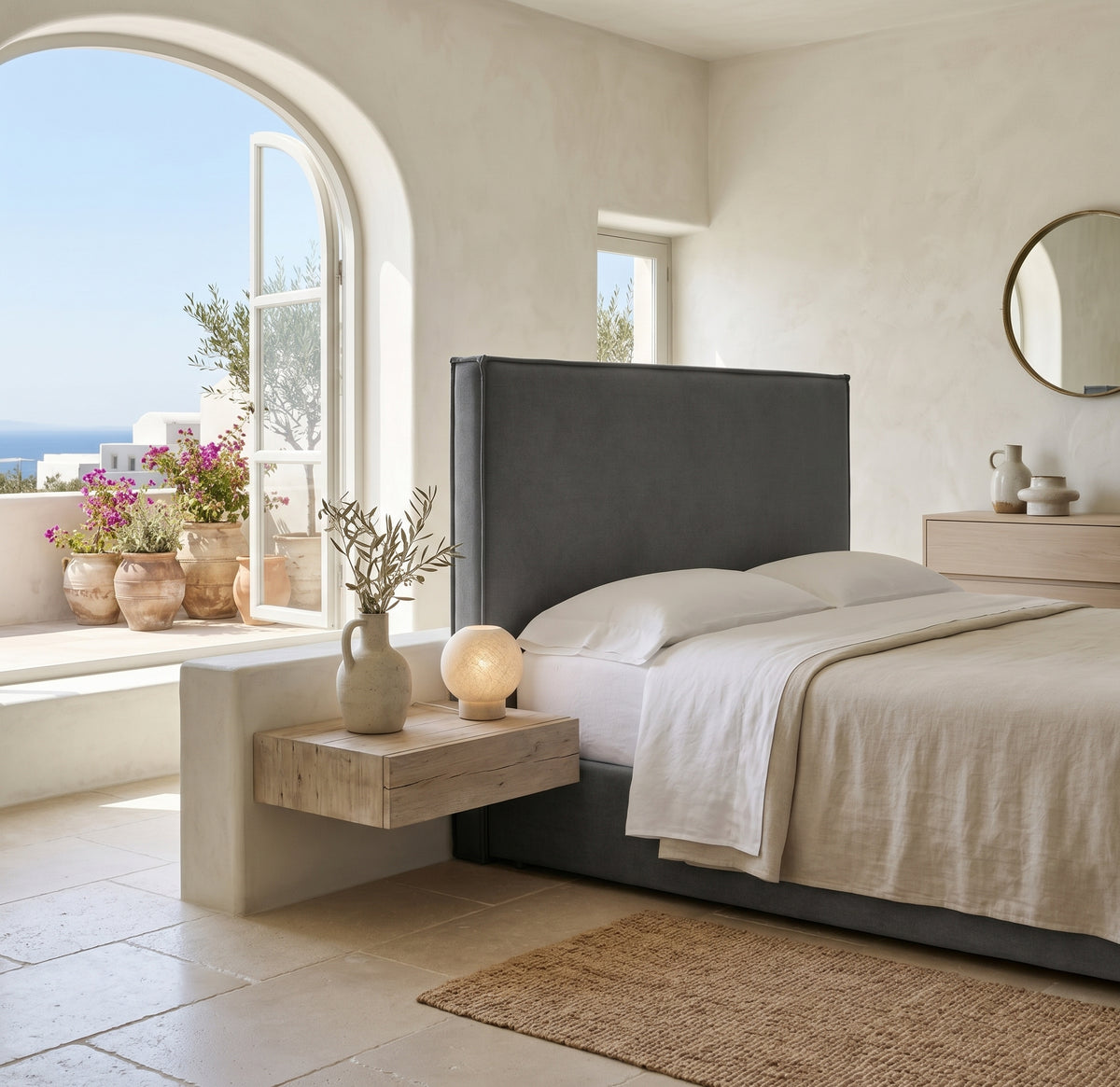Cabecero tapizado Mox antracita de Morfeo, liso con vivo, en un dormitorio mediterráneo con arco y vistas al mar.