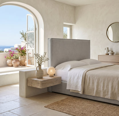 Cabecero tapizado Mox gris de Morfeo, liso con vivo, en un dormitorio mediterráneo con arco y vistas al mar.