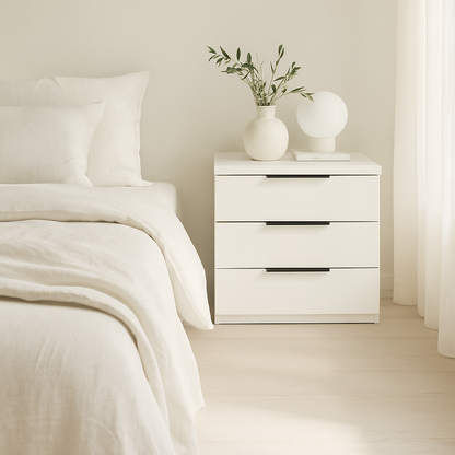 Mesita de noche Éter color blanco de Morfeo junto a una cama con ropa de lino blanca en un dormitorio luminoso.