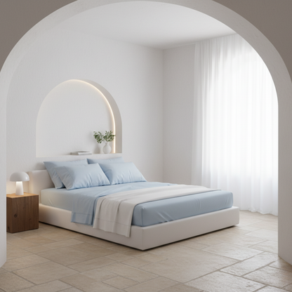 Juego de sábanas de algodón percal azul claro de Morfeo en dormitorio luminoso con cama vestida, almohadas y textiles blancos.