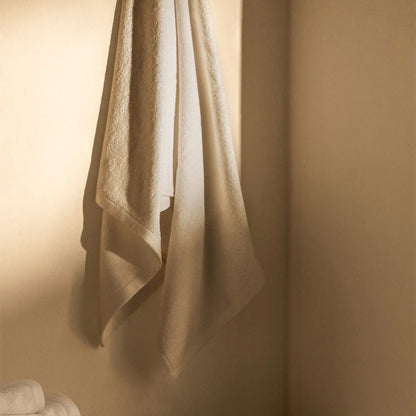 Toalla de baño Serena de Morfeo colgada en la pared de un baño con luz cálida.