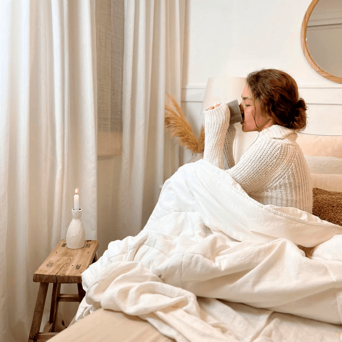 Mujer tomando una bebida caliente en la cama arropada con el edredón nórdico de bambú de Morfeo.