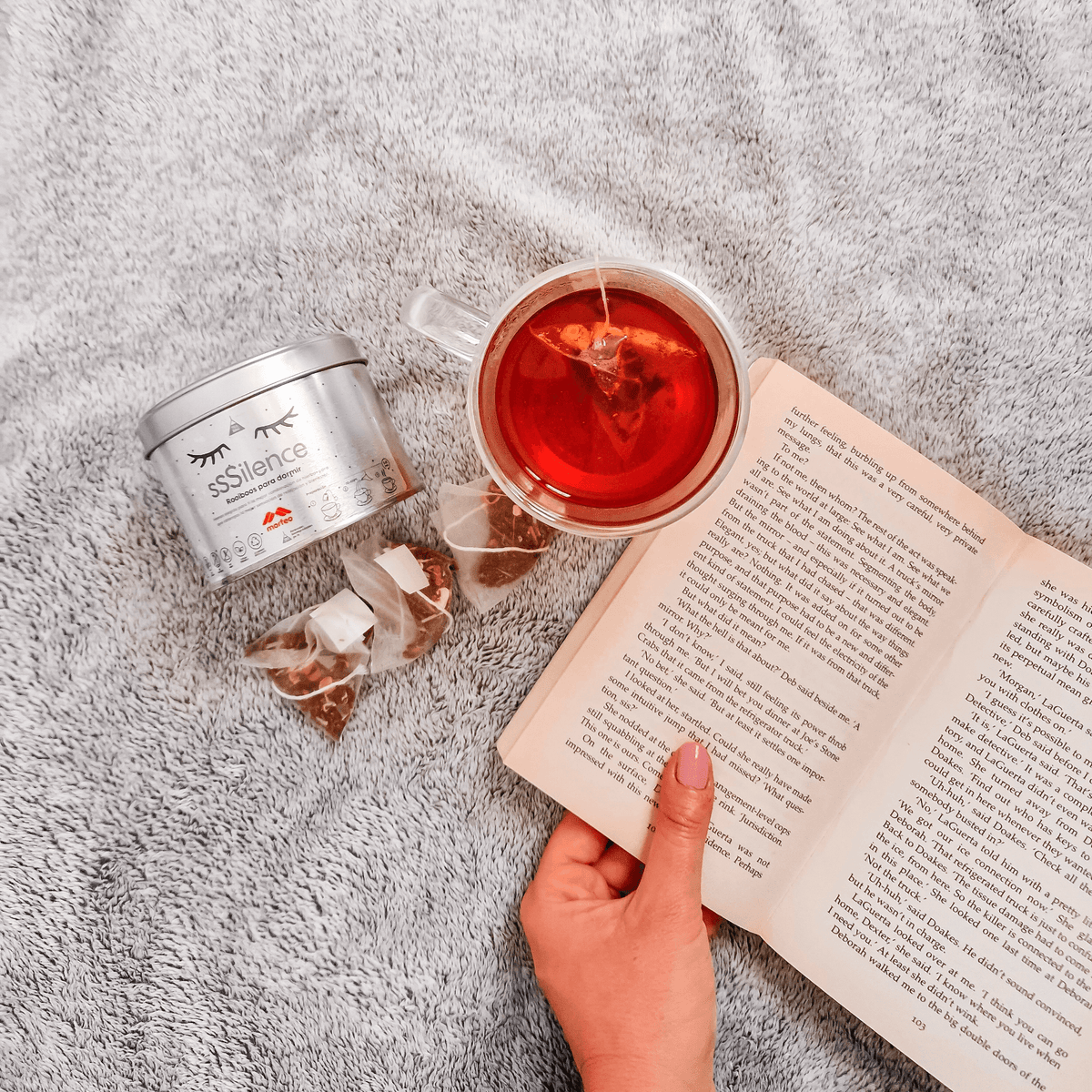 Rooibos relajante para dormir de Morfeo con taza de infusión y un libro abierto sobre una manta gris.