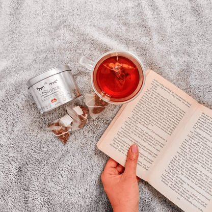Rooibos relajante para dormir de Morfeo con taza de infusión y un libro abierto sobre una manta gris.