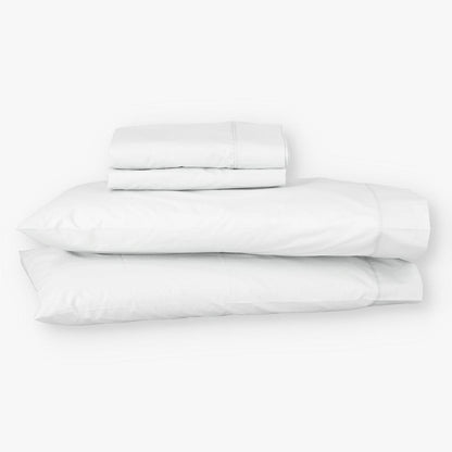 Juego de sábanas EcoPercal de algodón percal blanco de Morfeo doblado con sus fundas de almohada sobre fondo blanco.